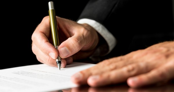 Closeup of male hand signing legal or insurance document on black desk with reflection.