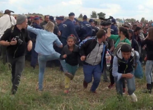 In this image taken from TV a Hungarian camerawoman, center left in blue, kicks out at a young migrant who had just crossed the border from Serbia  near Roszke Hungary Tuesday Sept. 8, 2015. The camerawoman has been fired after she was caught on video kicking and tripping migrants entering Hungary across the border with Serbia. The N1TV Internet channel said their employee, widely identified in Hungarian media as Petra Laszlo, has been dismissed because she "behaved unacceptably" at a makeshift gathering point where police take migrants immediately after they enter Hungary near the village of Roszke.(Index.Hu. via AP) HUNGARY OUT